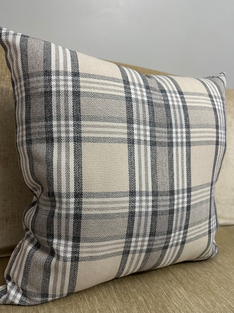 May include: A beige and gray plaid throw pillow with a square shape. The pillow has a subtle herringbone pattern within the plaid.