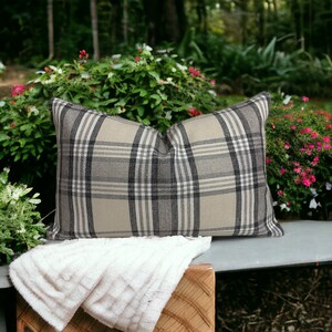 May include: A beige and black plaid throw pillow with a white throw blanket on a wooden bench.