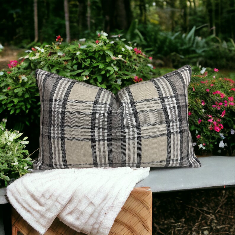 May include: A beige and black plaid throw pillow with a white throw blanket on a wooden bench.