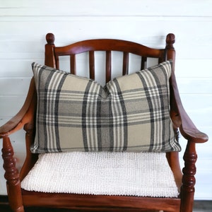 May include: A brown wooden chair with a white cushion and a plaid pillow. The pillow is beige and black with a checkered pattern.