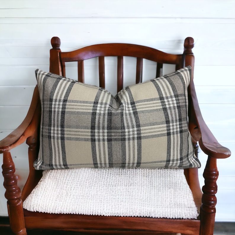 May include: A brown wooden chair with a white cushion and a plaid pillow. The pillow is beige and black with a checkered pattern.