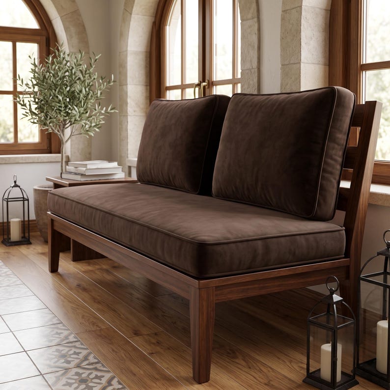 K&ouml;nnte beinhalten: Ein h&ouml;lzernes Zweisitzer-Sofa mit dunkelbraun gepolsterter Sitzfl&auml;che und zwei passenden R&uuml;ckenkissen. Der Rahmen besteht aus poliertem Holz mit einer R&uuml;ckenlehne aus Latten, die eine stabile Basis f&uuml;r die weichen Kissen bietet.