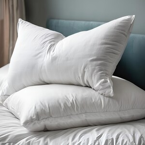 May include: Two white pillows on a bed with a blue headboard. The pillows are made of a soft, comfortable material and are perfect for sleeping.