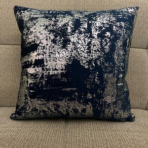 May include: A decorative throw pillow with a blue and silver abstract pattern. The pillow is made of a soft, plush fabric and has a square shape.