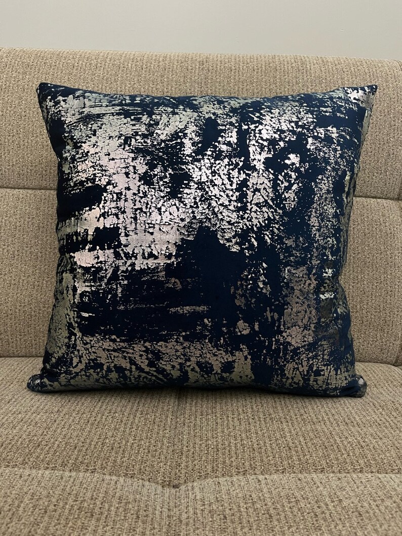 May include: A decorative throw pillow with a blue and silver abstract pattern. The pillow is made of a soft, plush fabric and has a square shape.