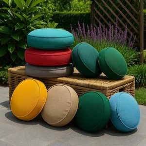 May include: A collection of round, textured cushions in various solid colors including turquoise, red, gray, yellow, beige, and shades of green. The cushions are arranged in a stack and placed upright on a woven wicker bench in an outdoor setting.
