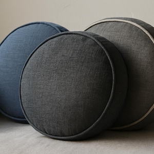 May include: Three round decorative pillows in shades of blue and gray. The pillows are arranged in a group, with the largest pillow in the back and the smallest in the front. The pillows have a textured fabric and a contrasting trim.