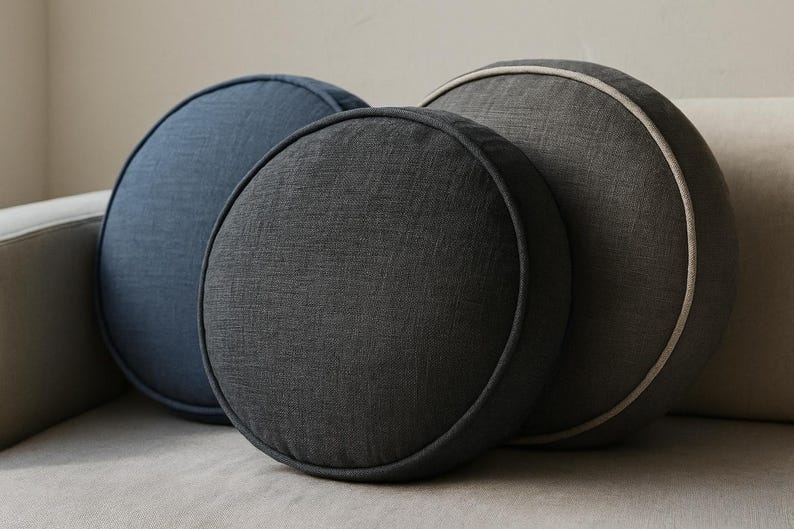 May include: Three round decorative pillows in shades of blue and gray. The pillows are arranged in a group, with the largest pillow in the back and the smallest in the front. The pillows have a textured fabric and a contrasting trim.