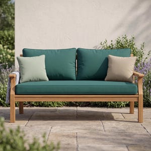 May include: A wooden outdoor loveseat featuring a natural light brown frame and deep teal cushions. The seating includes two large teal back cushions, one light green square throw pillow, one beige square throw pillow, and a patterned throw blanket.