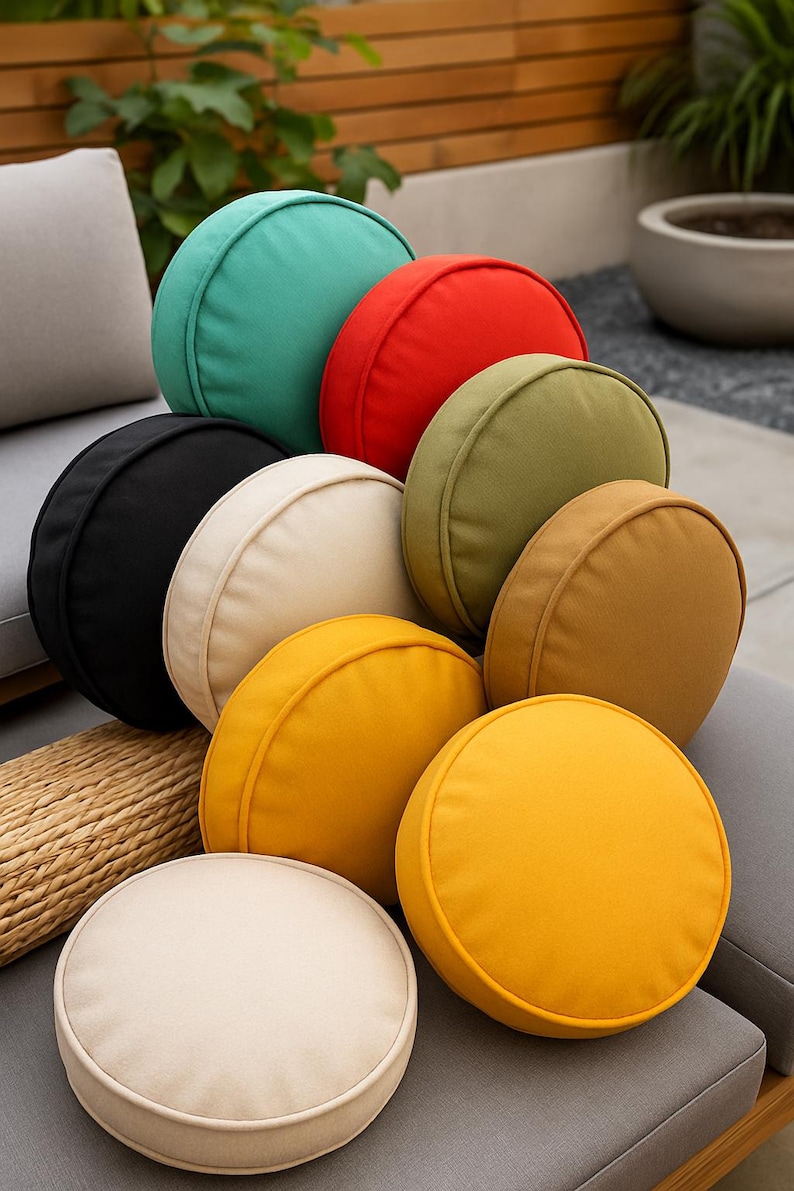May include: A collection of round, solid-colored throw pillows in various shades including teal, red, olive green, black, cream, tan, and bright yellow. Each cushion features a piped edge and a smooth fabric finish, arranged in a stacked cluster.
