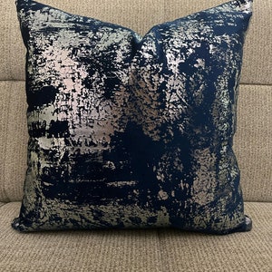 May include: A navy blue throw pillow with a silver metallic abstract design.