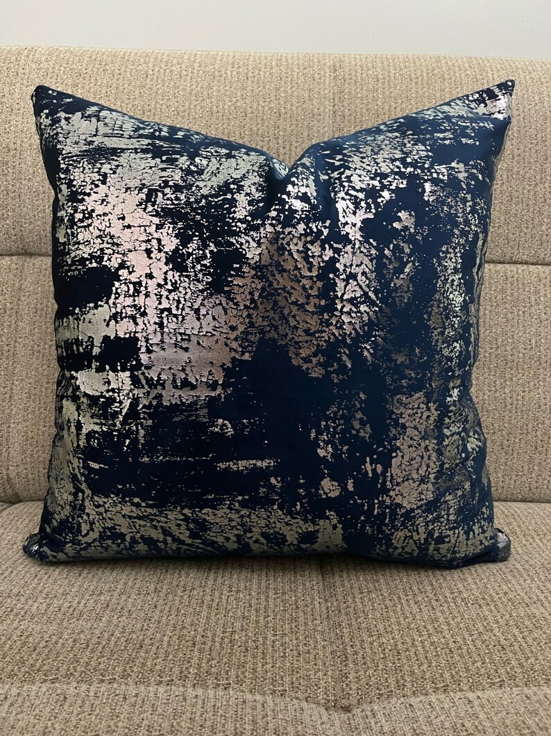 May include: A navy blue throw pillow with a silver metallic abstract design.