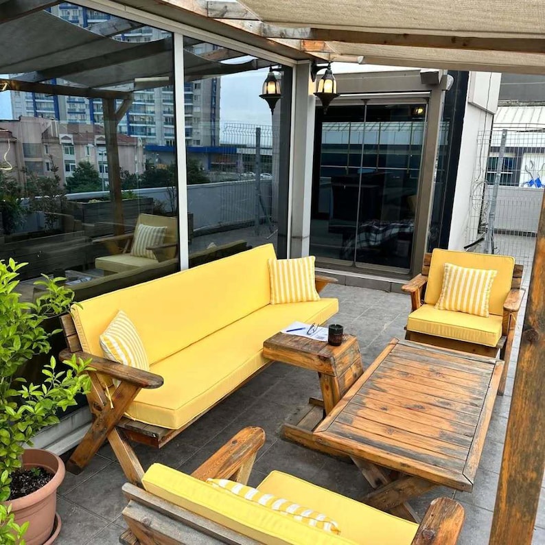 May include: A patio furniture set featuring a long sofa, two armchairs, and a rectangular coffee table, all crafted from dark wood. The seating includes bright yellow cushions and matching yellow and white striped throw pillows.
