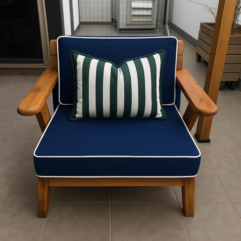 K&ouml;nnte beinhalten: Holz-Outdoor-Sessel mit marineblauen Kissen und einem gestreiften Kissen. Der Stuhl hat eine nat&uuml;rliche Holzoberfl&auml;che und wei&szlig;e Paspeln um die Kissen. Das Kissen hat vertikale gr&uuml;ne und wei&szlig;e Streifen.