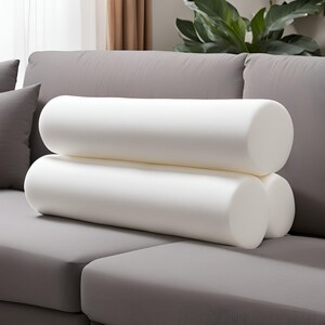 May include: Two white cylindrical pillows stacked on top of each other on a gray couch.