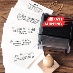 May include: A black self-inking rubber stamp and a wooden handle stamp positioned next to white envelopes printed with various return addresses including Thompson, Barington, Sophia & David, William & Olivia, and The Bennets, plus two gold paper clips.