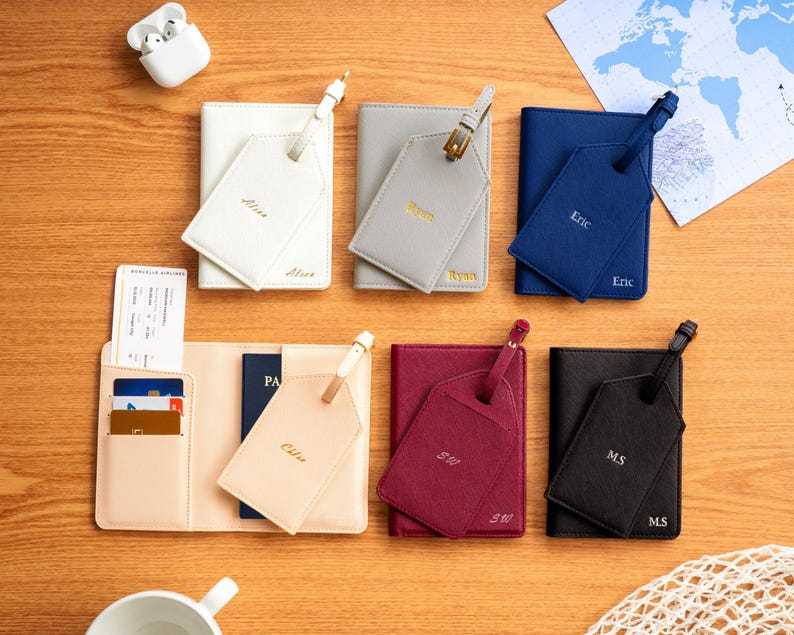 Puede incluir: Una colecci&oacute;n de accesorios de viaje personalizados, que incluyen portapasaportes y etiquetas de equipaje, en varios colores como blanco, gris, azul marino, burdeos y negro. Cada art&iacute;culo est&aacute; grabado con un nombre o iniciales en letras doradas.
