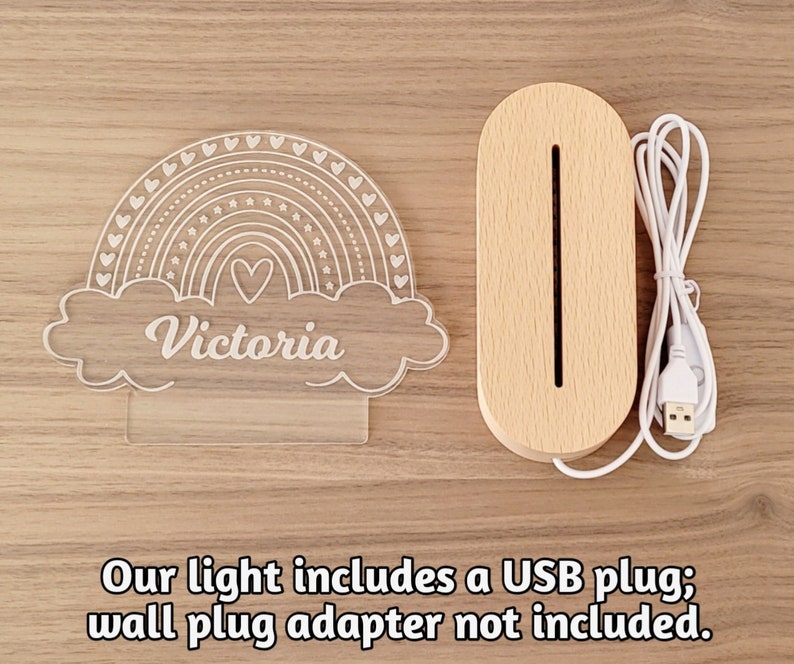 May include: A white acrylic rainbow night light with the name "Victoria" inscribed in the cloud. The light is plugged into a wooden base with a USB cord.