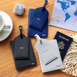 Puede incluir: Una colecci&oacute;n de accesorios de viaje, que incluye un tarjetero y etiqueta de equipaje azul marino con "Eric" impreso, un tarjetero y etiqueta de equipaje negro con "M.S" impreso y un tarjetero y etiqueta de equipaje gris con "Ryan" impreso.