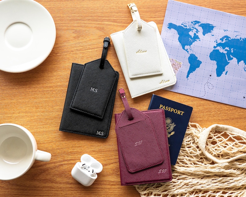 Puede incluir: Vista cenital de tres portapasaportes y etiquetas de equipaje personalizados en negro, blanco y burdeos. Cada soporte tiene una etiqueta a juego con iniciales. Tambi&eacute;n se ven un pasaporte y un mapa del mundo.