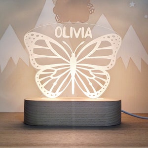 May include: A white butterfly-shaped night light with the name "Olivia" inscribed on the top. The light is on a wooden base.