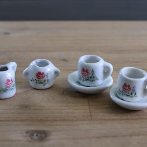 May include: A miniature tea set with a white teapot, creamer, sugar bowl, and two teacups with floral designs. The set is made of ceramic and has a delicate, vintage look.