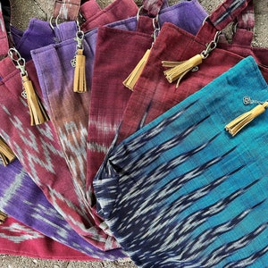 Può includere: Una collezione di borse tote colorate con un motivo ikat unico e nappine in pelle. Le borse sono realizzate in un tessuto morbido e tessuto e hanno una chiusura a zip.