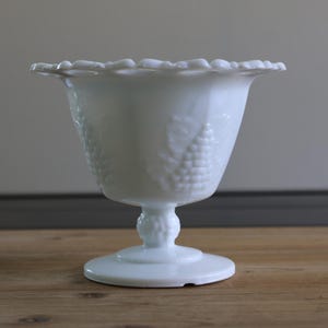 Könnte beinhalten: Weiße Milchglas-Fußschale mit gewelltem Rand und Traubenmuster.