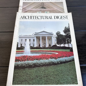 Może przedstawiać: Dwa egzemplarze magazynu Architectural Digest, międzynarodowego czasopisma poświęconego wysokiej klasy projektowaniu wnętrz. Numer z grudnia 1981 roku zawiera zdjęcie Białego Domu z fontanną i czerwonymi kwiatami na pierwszym planie.