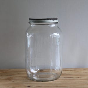 Op de afbeelding: Een grote, heldere glazen pot met een wit deksel. De pot is leeg en heeft een brede opening.