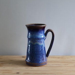 May include: A blue and brown ceramic mug with a wide base and a handle. The mug has a mottled glaze with shades of blue and purple.