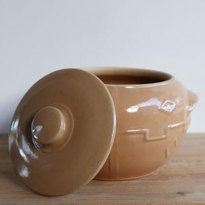 Może przedstawiać: Brązowa ceramiczna naczynie do zapiekania z pokrywką. Naczynie ma ozdobny wzór na boku i gałkę na pokrywce.