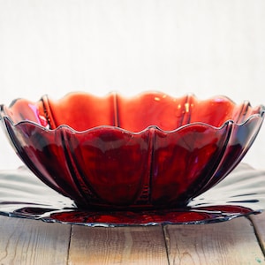 Peut inclure: Un grand bol de service en verre rouge foncé avec une assiette assortie. Le bol a un bord festonné et l'assiette a un bord ondulé.