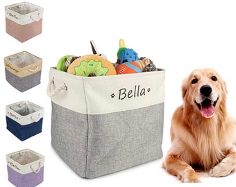 May include: A gray and white canvas storage bin with rope handles. The bin is filled with dog toys and has the name "Bella" embroidered on the front. A golden retriever dog is lying on the floor next to the bin.