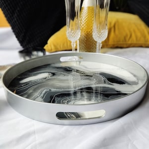 May include: A silver tray with a black and white marbled design and glitter accents. The tray has two handles on the sides.