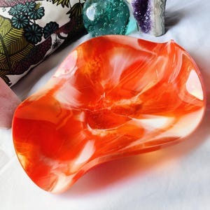 May include: A large, orange and white resin bowl with a wavy, organic shape. The bowl is made with a swirling, marbled effect.