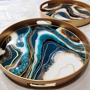 May include: Two round gold trays with a white, blue and gold abstract design. The design resembles swirling marble or agate.
