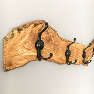 May include: A wooden coat rack featuring four black metal hooks. The wood is a natural light brown with visible grain and knots. The hooks are curved and have a decorative circular element. The rack is designed for wall mounting.