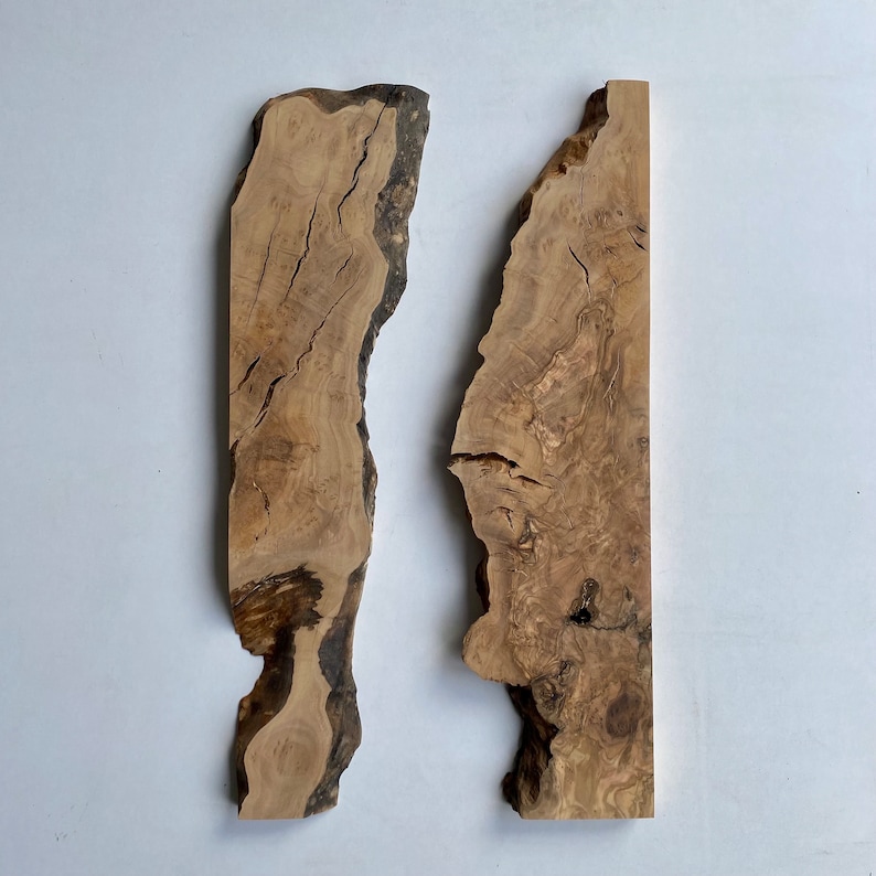 May include: Two irregularly shaped, light brown wooden slabs with dark brown edges and visible wood grain. The slabs are positioned side by side against a white background. The wood has natural cracks and variations in colour.
