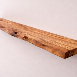 May include: A rectangular wooden shelf featuring a natural live edge along the front side. The wood displays a prominent grain pattern with warm brown and golden tones, showcasing the organic texture and knots inherent to the timber material.