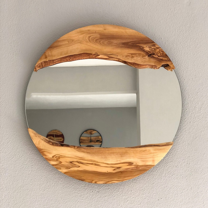 May include: Round mirror with a natural wood frame. The frame is made of light brown wood with a unique grain pattern. The mirror is mounted on a light gray wall.