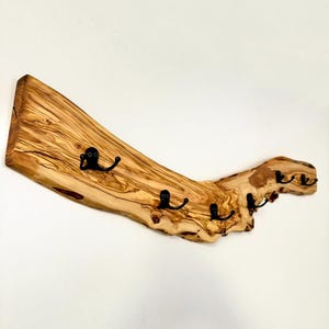May include: A rustic wooden coat rack with four black metal hooks. The rack is made from a piece of natural wood, showcasing its unique grain and texture. The wood has a light brown color with darker streaks.