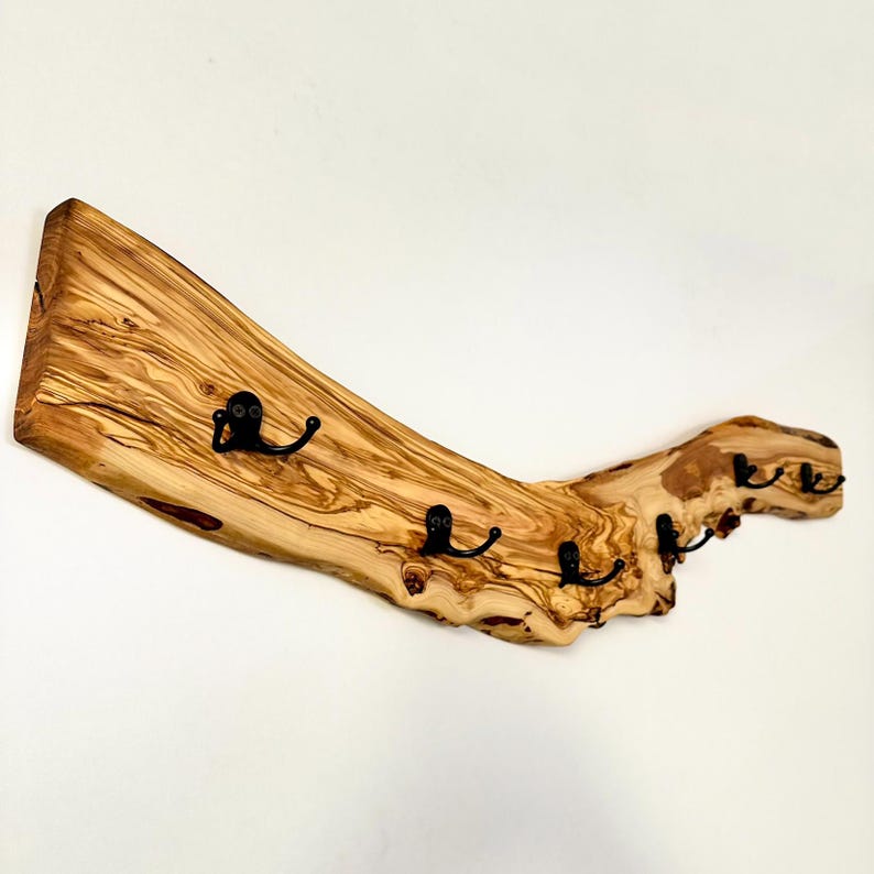 May include: A rustic wooden coat rack with four black metal hooks. The rack is made from a piece of natural wood, showcasing its unique grain and texture. The wood has a light brown color with darker streaks.