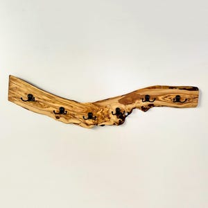 May include: A wooden coat rack with five black metal hooks. The rack is made from a piece of light brown wood with a natural, curved shape. The wood has a visible grain and knots, adding to its rustic appeal. The hooks are evenly spaced along the bottom edge.