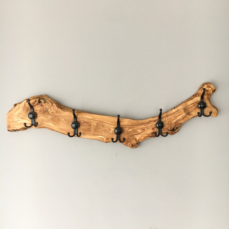 May include: A rustic wooden coat rack made from a natural olive branch. It features six black metal hooks evenly spaced along the curved, light brown wood. The wood grain is visible, adding to the natural aesthetic. A decorative and functional wall hanging.