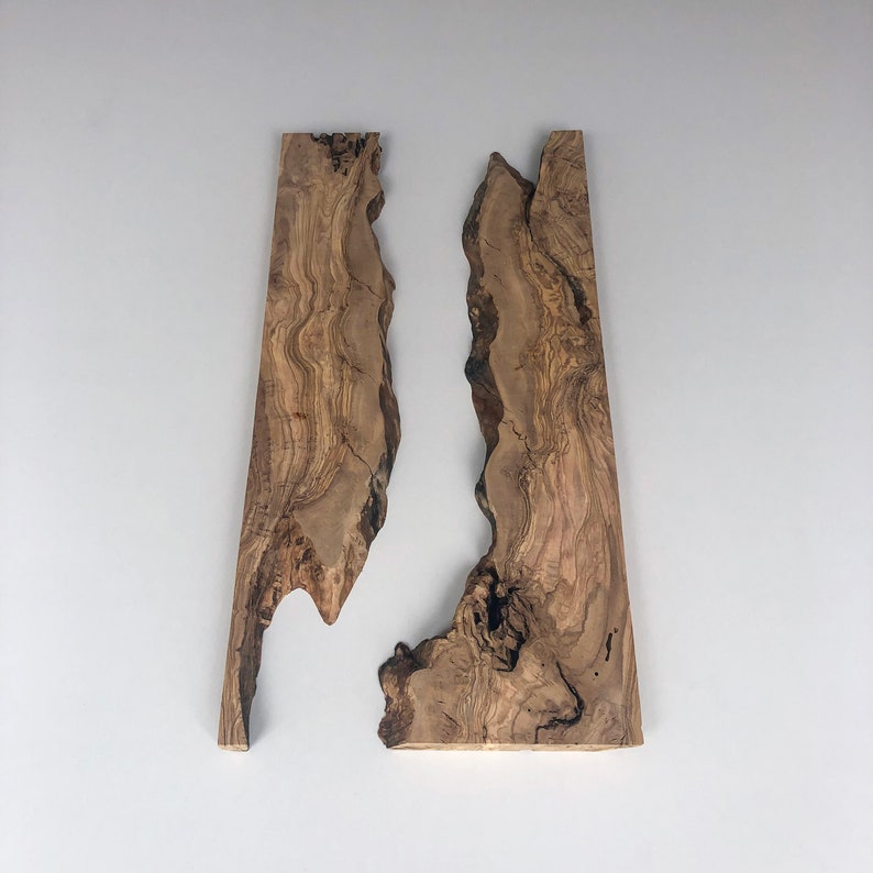May include: Two irregularly shaped wooden planks with a natural, organic edge. The wood grain features a mix of light and dark brown tones, creating a textured appearance. The planks are likely for woodworking or craft projects.