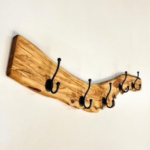 May include: A wooden coat rack with six black metal hooks. The rack is made from a light-colored, natural wood slab with a unique, organic shape. The hooks are evenly spaced along the bottom edge.