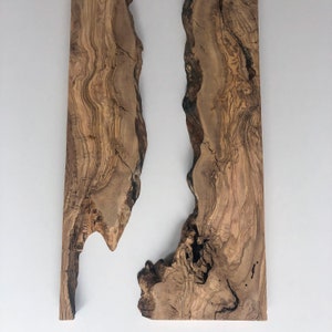 May include: Two vertical, irregularly shaped wooden planks with a natural, light brown color and visible wood grain. The planks are set against a plain white background, showcasing their organic forms and textures. The wood has dark brown streaks.