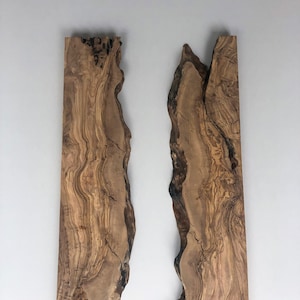 May include: Two vertical wooden slabs with natural, irregular edges. The wood grain features a mix of light and dark brown tones, with visible knots and patterns. The slabs are displayed against a plain white background, highlighting their organic texture.