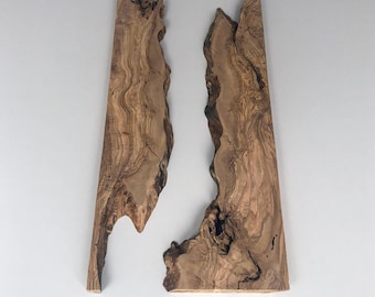 May include: Two irregularly shaped wooden slabs with natural edges. The wood has a warm brown color with intricate grain patterns and dark streaks. The slabs are displayed against a plain white background.